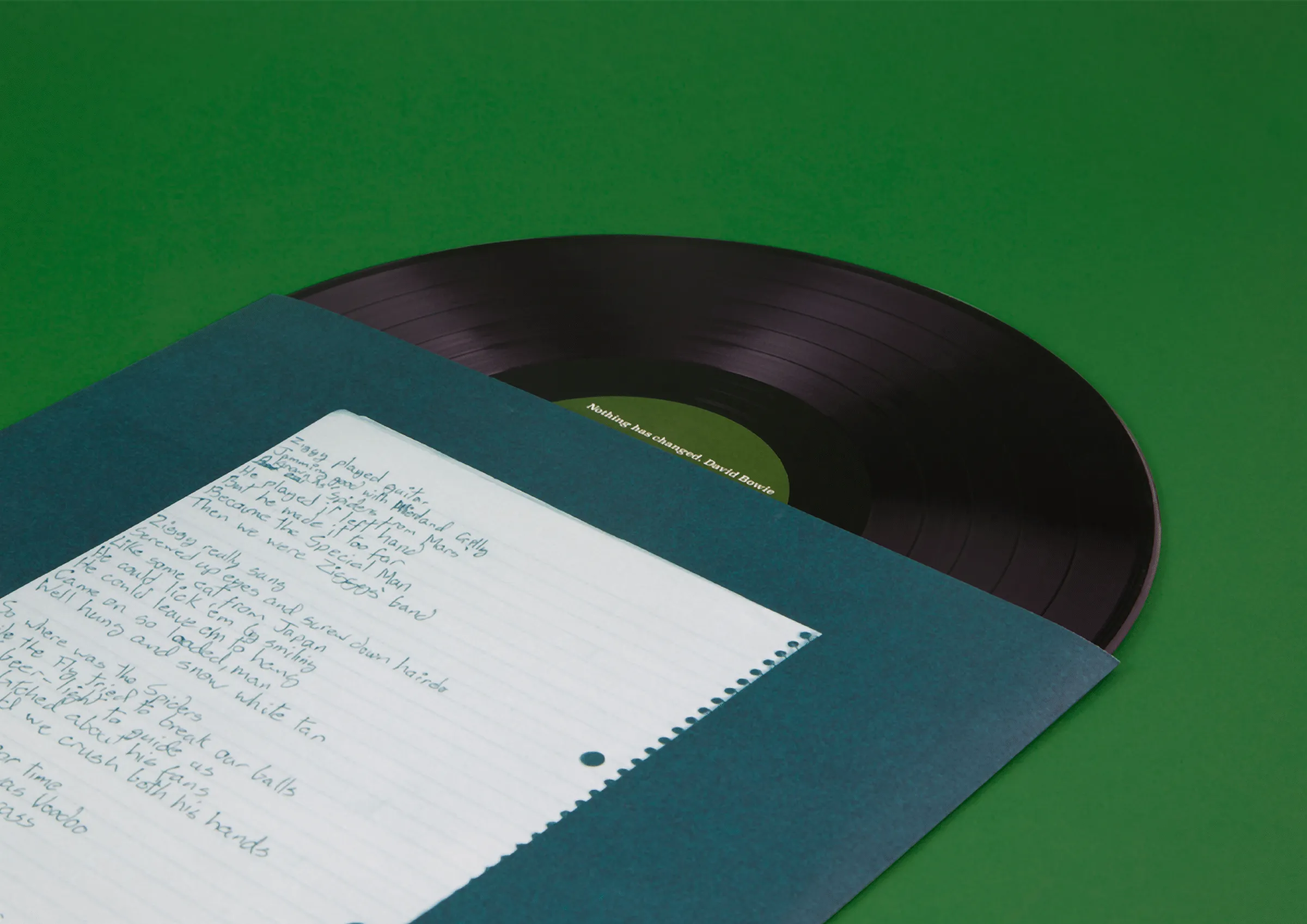 Vinyl record sliding out of a teal sleeve holding handwritten lyrics, on a green background