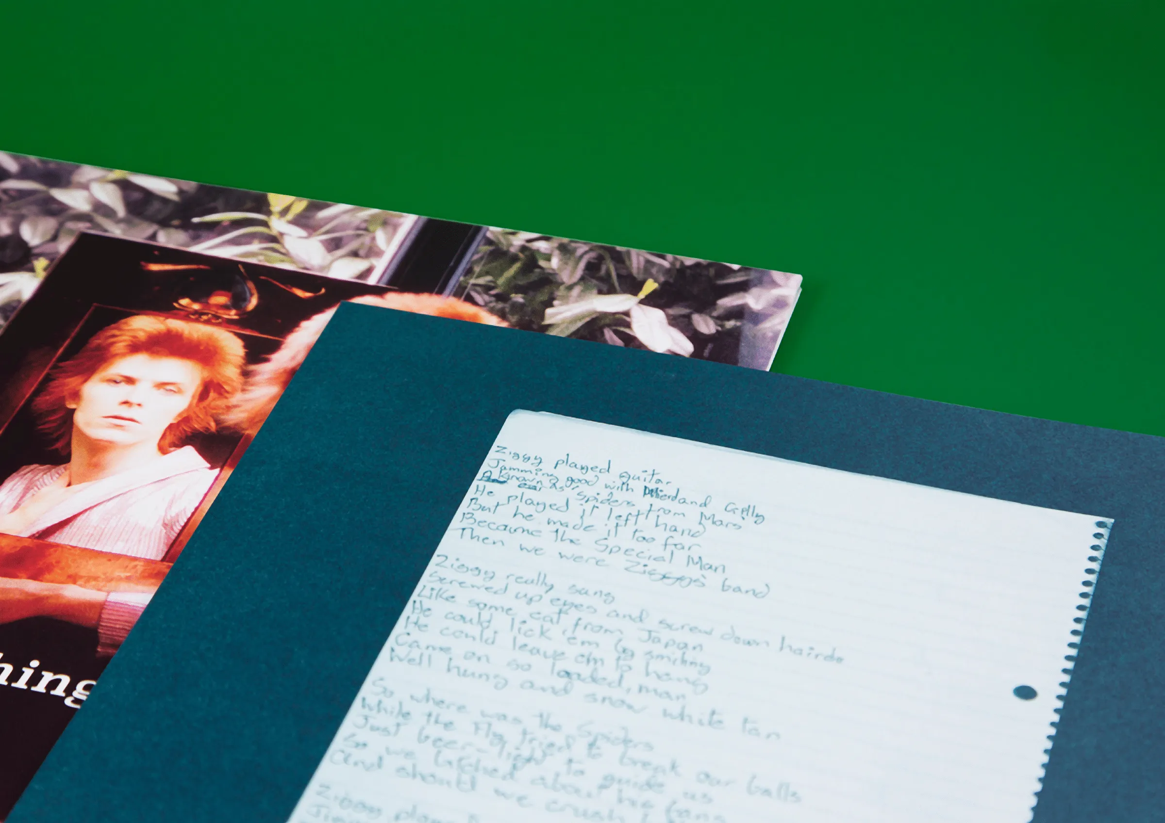 Handwritten lyrics on lined paper over a teal sleeve and a portrait of David Bowie, on a green background